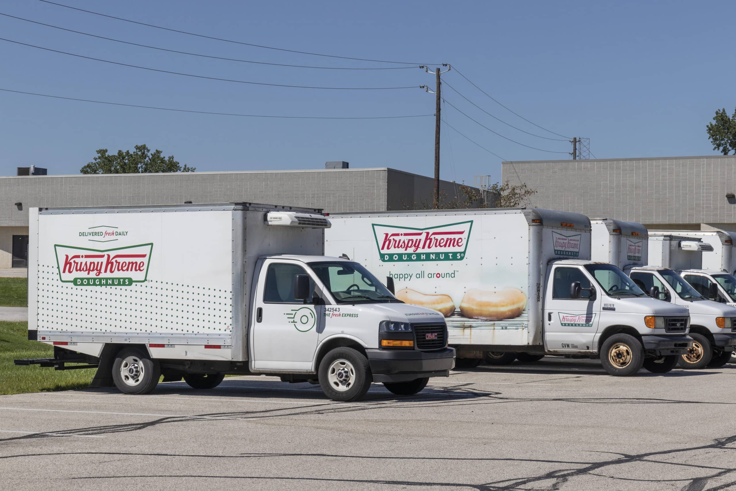 Krispy Kreme trucks are parked in a parking lot on a sunny day