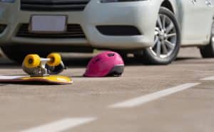 A yellow skateboard and a pink helmet are laying in the street after a skateboarder was struck by a car in an accident