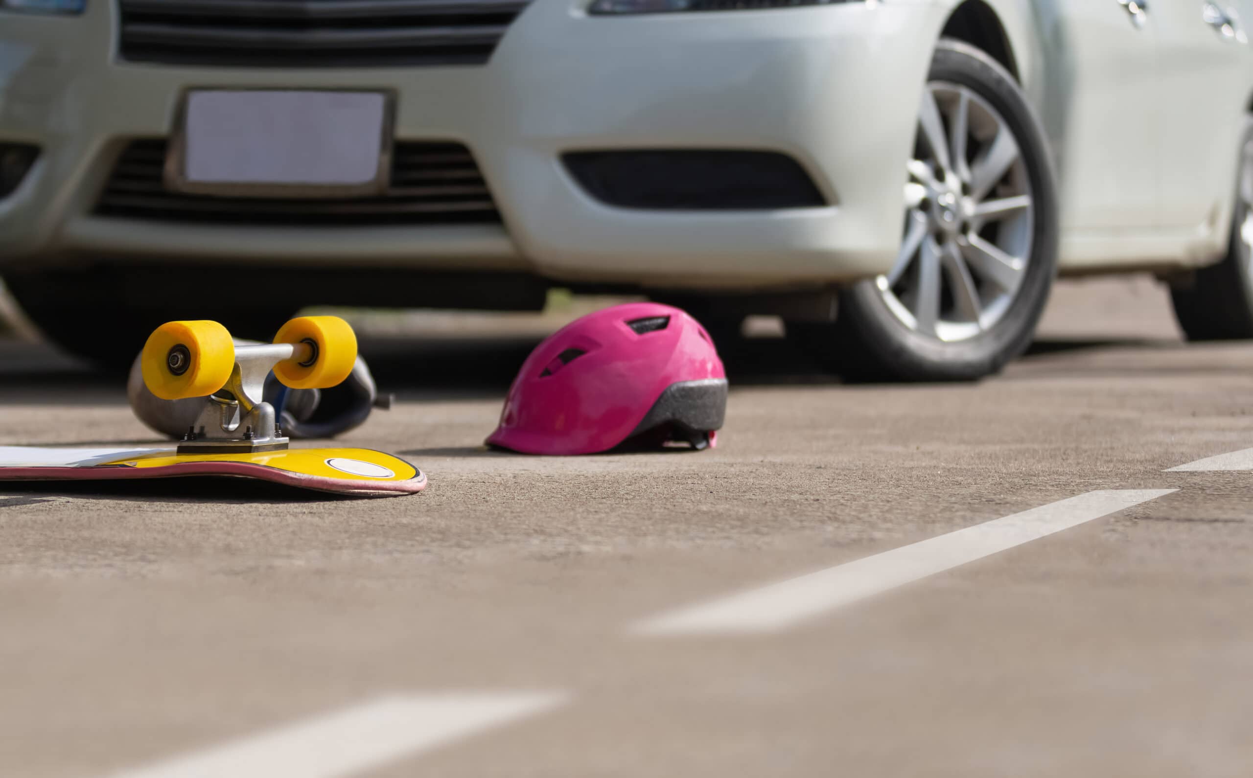 A yellow skateboard and a pink helmet are laying in the street after a skateboarder was struck by a car in an accident